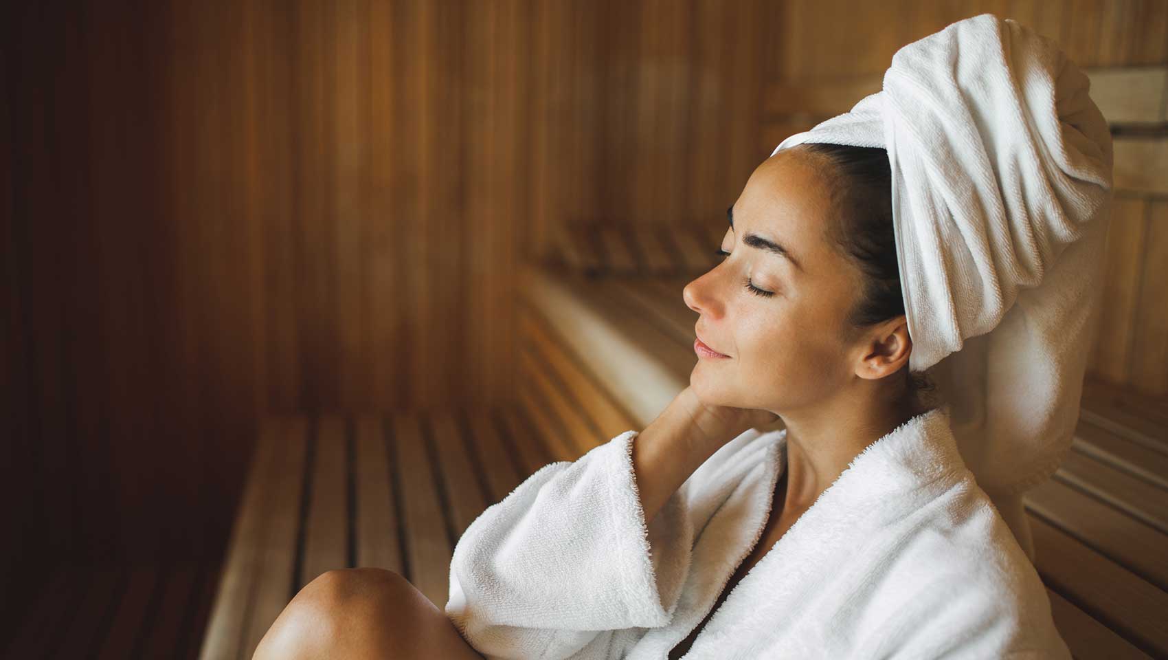 woman relaxing in a sauna and wearing a robe and also a towel on her head